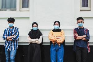 Group of teens with their backs leaning on wall and folded arms wearing masks to protect themselves from the coronavirus together photo