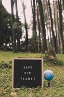 Quote on letter board says Save Our Planet with earth globe with forest background, earth day concept photo