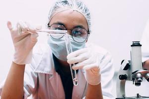 mujer científica con máscara protectora y guantes que vierten sustancia líquida en el tubo de ensayo en el laboratorio químico científico. día nacional de la ciencia, día mundial de la ciencia foto