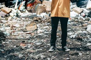 A man standing in trash dump or landfill with messy garbage dump pile on background