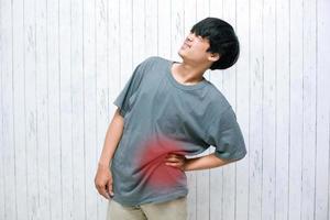 Asian young man holding her aching back, the concept of back pain, lactic acid in muscles and spinal problems, lumbago photo