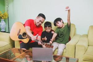 Asian father with guitar smiling together to laptop with his son photo