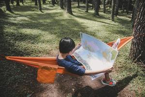 un niño acostado en una hamaca en la jungla mientras mira un mapa de papel, un niño aventurero foto