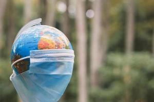 Earth globe in medical mask with blurred nature background. Wearing face mask. photo