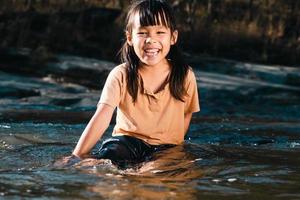 Asian little girl playing in the forest stream. Active recreation with children on river in summer. photo