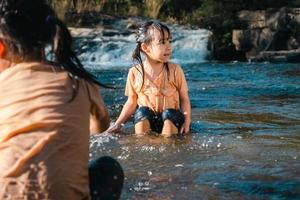 Asian little girl playing in the forest stream with her sister. Active recreation with children on river in summer.