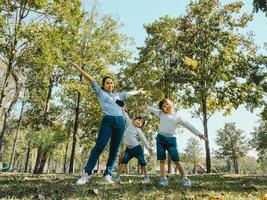 Two cute little Asian girls in summer outfits, having fun with a beautiful young mother smiling happily in the park. Motherhood and family concept. photo
