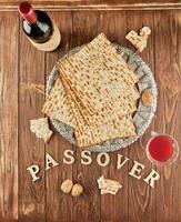 Pesach celebration concept - Jewish holiday Pesach. Matzah on traditional Seder plate with bottle of red wine, glass of wine and nuts on wooden background and the inscription passover photo