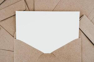 se coloca papel blanco en blanco en el sobre de papel marrón abierto. maqueta de tarjeta de felicitación en blanco horizontal. vista superior del sobre de papel artesanal sobre fondo blanco. plano de papelería. estilo minimalista.