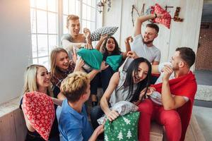 Crazy young best friends fighting pillows at home. Mixed race group of people. Concept  entertainment and lifestyle photo