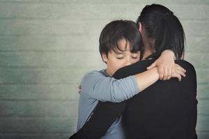 niño triste abrazando a su madre foto