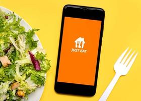 Just eat application icon on black screen of smartphone with lettuce salad plate and white plastic fork photo