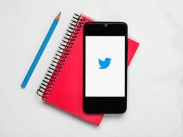 Twitter application icon on white screen of smartphone with notebook and blue pencil photo