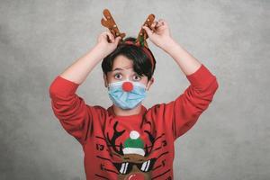 feliz navidad, niño divertido con máscara médica en un disfraz de navidad de reno rudolph foto