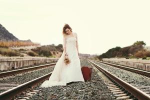 Pensive bride with a red suitcase on the train tracks photo