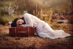 young woman sitting in the field with suitcase photo