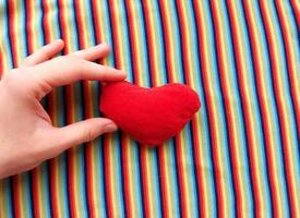 red heart in hand on a background of rainbow fabric. place for text. bright banner, concept. love. copy space. photo
