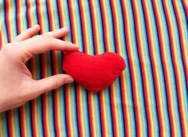 red heart in hand on a background of rainbow fabric. place for text. bright banner, concept. love. copy space. photo