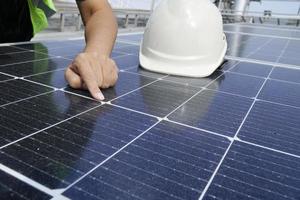 un ingeniero eléctrico con un sombrero blanco está comprobando. Limpieza de paneles solares en el techo del edificio. foto