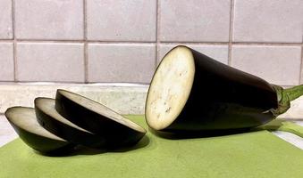 Slices eggplant on a green cutting board against the background of a beige wall close-up photo