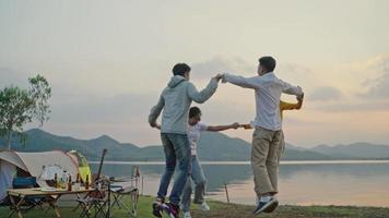 grupp fyra personer vänner asiatiska män och kvinnor camping picknick firar att hålla händerna i en cirkel och dansa ha kul och njuta av marken tält. reservoarområde under solnedgångens semestertid. video