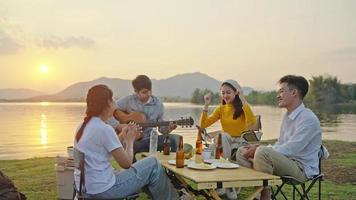 Group Four People Friends Asian men and women Camping, drinking beer, celebrating, Singing, Playing Guitar, Having fun and Enjoying Ground tent. Reservoir area during Sunset Vacation Time. video