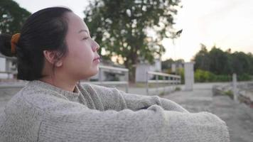 Asian woman sitting and getting good weather by the river. Getting some fresh air. Sitting by the river.Trees background, looking beautiful view in the evening video