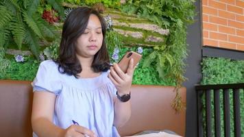 mujeres asiáticas sentadas y trabajando en un café y tomando un teléfono, mujer de negocios tratando de escribir ideas y planes de negocios de inicio en el café, pensamientos creativos para escribir en un cuaderno. creando el concepto de lista video