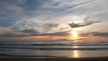 belo pôr do sol na praia com nuvens. oceano e ondas calmas. cores pastel agradáveis. momento calmo e relaxante. video