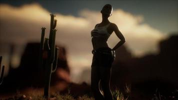 mulher de camisa rasgada em pé por cacto no deserto ao pôr do sol