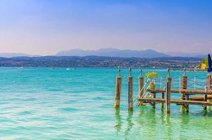 Garda lake with blue azure turquoise water and wooden pier dock, coast with mountain range
