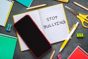 dejar de intimidar vista superior del cuaderno con el texto detener el acoso escolar, útiles escolares y teléfono inteligente foto
