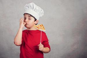 niño divertido cocinar con rebanada de pizza foto