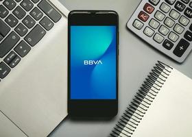 BBVA mobile app logo on smartphone screen next to a notebook, laptop and calculator photo