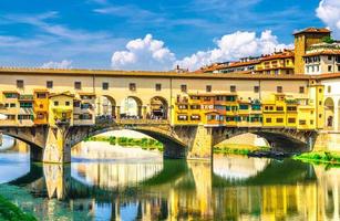 Ponte Vecchio stone bridge with colourful buildings houses over Arno River blue reflecting water photo