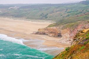 Top aerial view of sandy beach with rocks and cliffs and waves of azure turquoise water of Atlantic Ocean near Nazare town photo