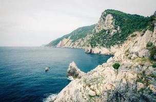 Grotta di Lord Byron with blue water, coast with rock cliff, yellow boat and blue sky near Portovenere town photo