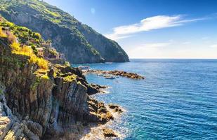 Rocks and cliffs coastline of Riviera di Levante of National park Cinque Terre Coast, Ligurian and Mediterranean Sea with blue sky in sunny day, copy space, Riomaggiore village, Liguria, Italy