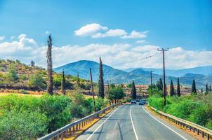 Landscape of Cyprus with cars vehicles riding asphalt road in valley with yellow dry fields, cypress trees and roadside poles photo