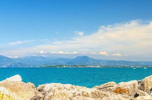 View from stone pier mole of Garda Lake azure water with Monte Baldo mountain range and Sirmione peninsula