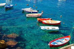 Fishing colorful multicolored boats on transparent clear water with visible bottom in small stone harbor of Riomaggiore village National park Cinque Terre coast, Ligurian and Mediterranean Sea, Italy photo