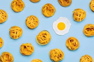 Top view of creative pattern made of raw tagliatelle nests pasta and a fried egg photo