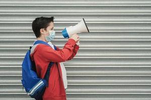 niño con máscara médica y mochila gritando con megáfono de regreso a la escuela foto