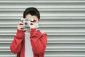 niño con máscara médica toma fotos con su cámara