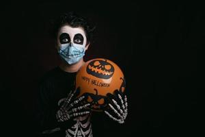 feliz halloween, niño con máscara médica disfrazado de esqueleto con globo de halloween foto