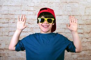 niño feliz y sonriente con gorra y gafas de sol mostrando las palmas de las manos foto