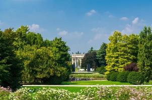 Arch of Peace gate and green trees, grass lawn in park, Milan, Italy