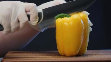 vegano experimentado corta cebolla morada con un cuchillo de acero grande en una tabla de madera marrón bajo una luz eléctrica brillante en un primer plano extremo video