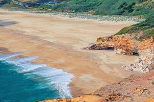 Top aerial view of sandy beach with rocks and cliffs and waves of azure turquoise water of Atlantic Ocean near Nazare town photo