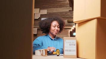 Afro-Amerikaanse vrouwelijke werknemer in veiligheidsuniform met behulp van streepjescodescanner om verzendorders te controleren in het pakhuis, papierfabriek voor de verpakkingsindustrie, logistieke transportservice.